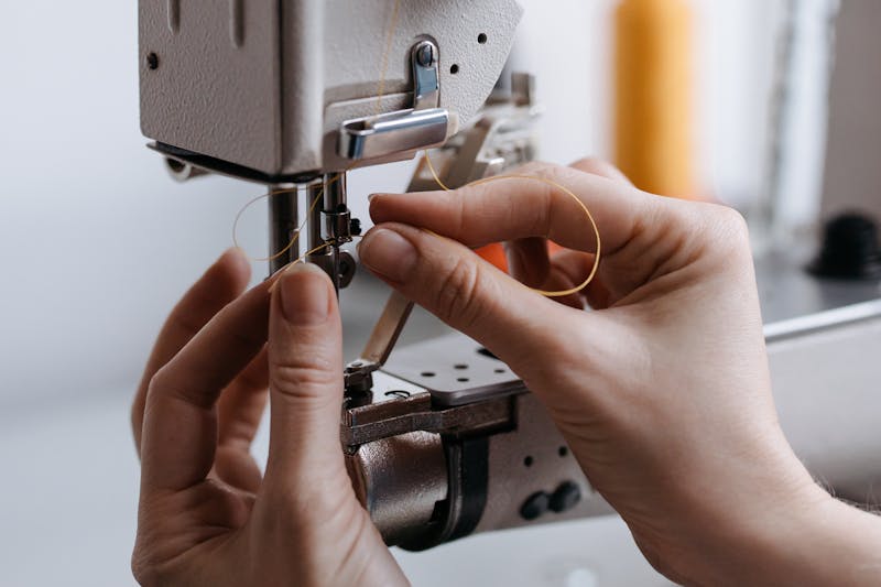 Close-up of hands threading industrial sewing machine for stitching work