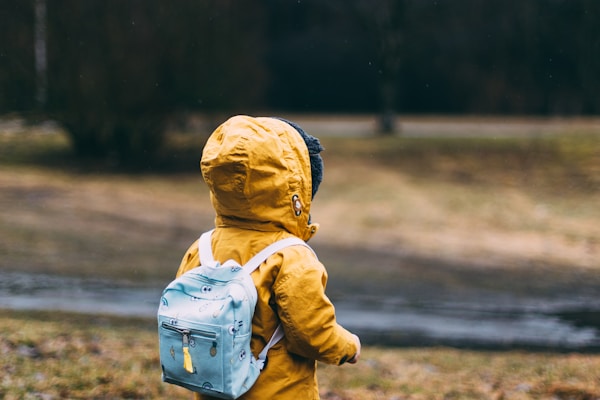 Child wearing warm yellow winter jacket with backpack outdoors